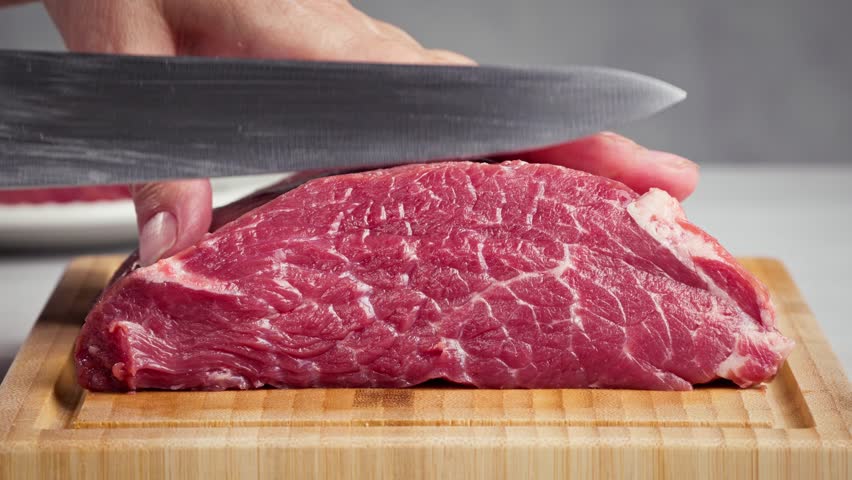 chef cut meat on cutting board with sharp knife for making healthy meal and cooking, chef cutting raw meat into pieces, slicing for steak. Beef fillet langet, food closeup