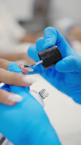 Beautician carefully painting client's fingernails white in nail salon, providing professional manicure service
