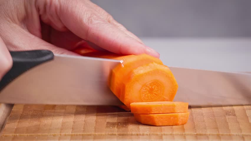chef cut carrot on cutting board with sharp knife for making healthy meal and cooking, cook cutting carrots for making salad, food closeup in kitchen