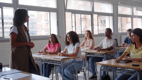A female teacher walks between desks in a classroom and approaches a student to clarify doubts, fostering interaction, guidance and academic support during the lesson. - Powered by Shutterstock - Get 15% off with code: PIKWIZARD15