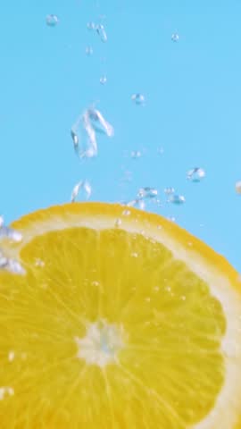 Sliced orange fruit drop underwater on blue background. Citrus freshness with splash and bubbles. Summer refreshment and juicy taste. Healthy vitamin drink and seasonal harvest moment