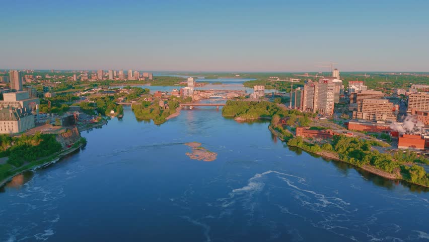 Aerial view over the Ottawa River, dividing Ottawa, Ontario, and Hull, Quebec. The vibrant cityscapes are bathed in early morning light, reflecting in the calm waters