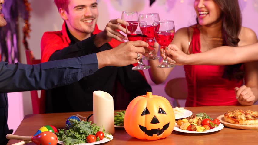 Asian friends in creative Halloween costumes gather on a sofa under colorful RGB lights, laughing and enjoying a festive night party filled with spooky decorations, joy, and playful holiday spirit.