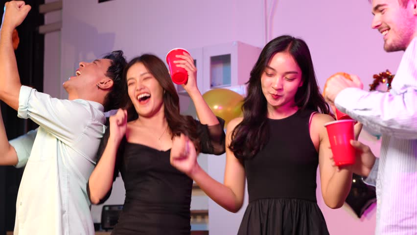 Asian friends in creative Halloween costumes gather on a sofa under colorful RGB lights, laughing and enjoying a festive night party filled with spooky decorations, joy, and playful holiday spirit.