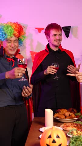 Asian friends in creative Halloween costumes gather on a sofa under colorful RGB lights, laughing and enjoying a festive night party filled with spooky decorations, joy, and playful holiday spirit.