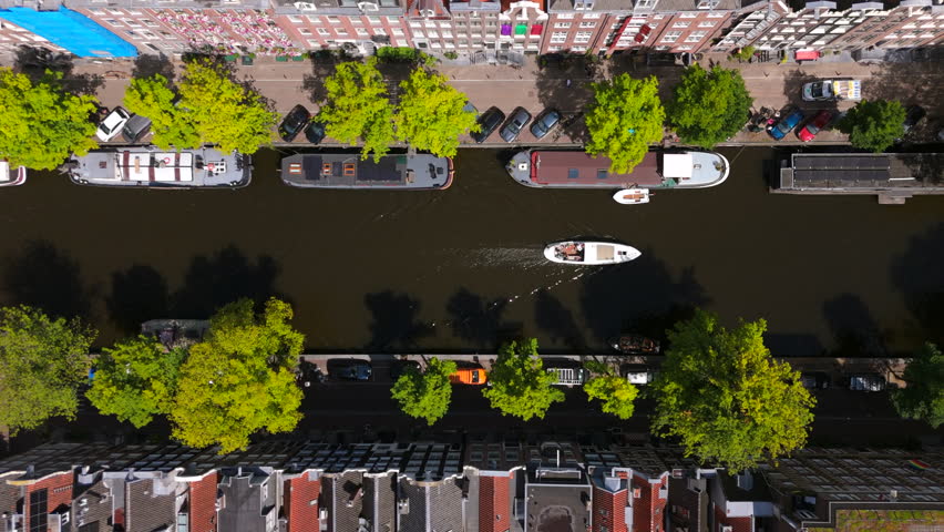 Take a moment to enjoy a breathtaking aerial view of the beautiful canals of Amsterdam, where vibrant trees frame picturesque waterways and iconic historic houses line the banks majestically