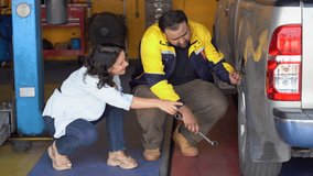 An experienced Indian male auto mechanic in a professional uniform is explaining a tire inspection to a Caucasian female customer. customer service in a modern garage, maintenance and repair - Powered by Shutterstock - Get 15% off with code: PIKWIZARD15