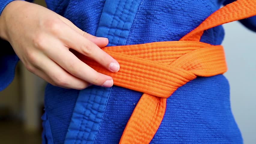 A detail of a blue judo tracksuit tied with an orange belt, demonstrating martial arts training. Rules for tying a belt.