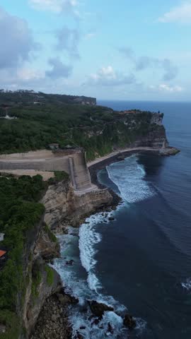 17s vertical 4K drone pullback showing rocky cliffs and clear blue ocean with white waves crashing, cinematic seascape in Uluwatu, Bali, Indonesia.