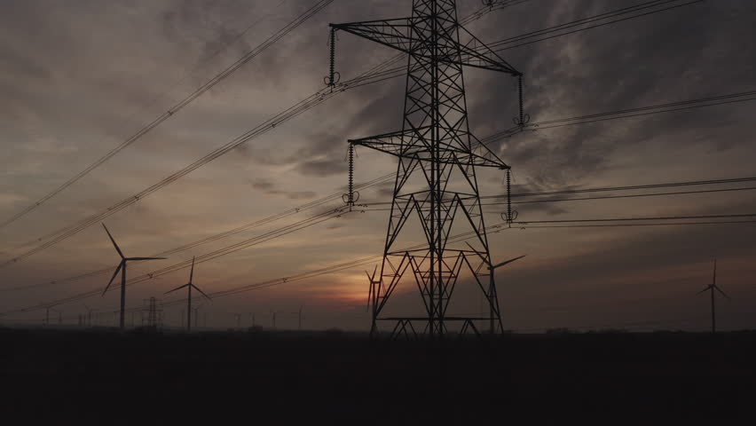 Aerial view in evening from drone of pylons cables and wind turbines providing power to North England. Sunset and green energy as renewable power is coming through electricity lines UK England 4K