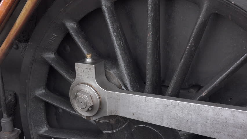 Close up of steam train wheels and smoke coming from pipes as locomotive gets ready to move from station. Transport traditional and old in a historic railway for tourism England UK 4K 