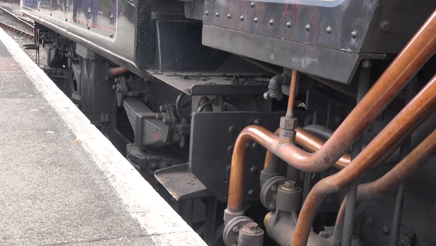 Close up of steam train wheels and smoke coming from pipes as locomotive gets ready to move from station. Transport traditional and old in a historic railway for tourism England UK 4K 