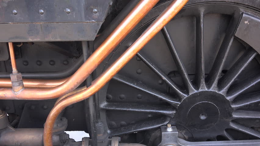 Close up of steam train wheels and smoke coming from pipes as locomotive gets ready to move from station. Transport traditional and old in a historic railway for tourism England UK 4K 