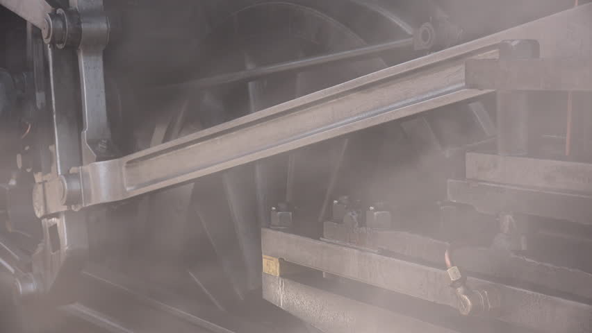 Close up of steam train wheels and smoke coming from pipes as locomotive gets ready to move from station. Transport traditional and old in a historic railway for tourism England UK 4K 