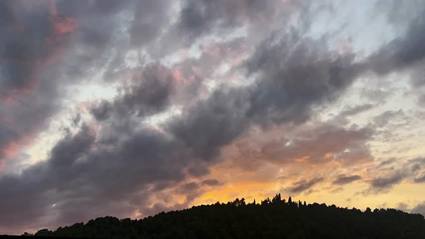 Stunning sunset over Mediterranean hills, clouds gently moving as the sky transforms into vibrant hues of orange and purple
