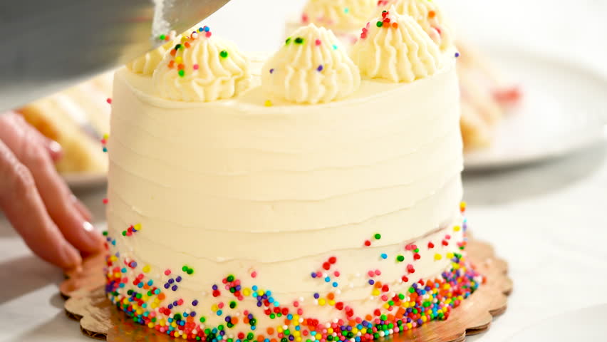 A detailed view highlights the creamy texture of the cake frosting and the colorful sprinkles around the base. The shot captures the smoothness of the piped decorations.