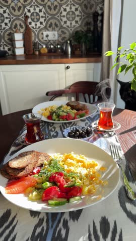 A cozy breakfast scene for two featuring scrambled eggs, a fresh side salad,  glasses of Turkish tea. A black cat relaxes nearby amidst lush indoor plants Making delicious salad with salted salmon