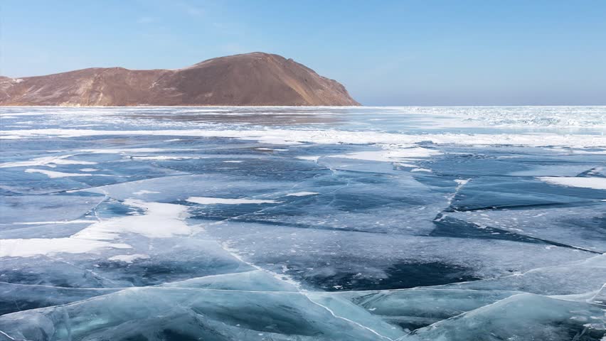 Panoramic video of winter landscape of frozen Baikal Lake with blue transparent ice with cracks on sunny cold day. Winter ice travels and outdoor recreation. Beautiful seascape. Natural background
