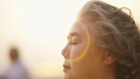 Close up of Asian senior woman face open an eyes while practicing meditation on the beach at summer sunset. Retirement elderly people enjoy outdoor relaxing carefree. Mental health care and motivation - Powered by Shutterstock - Get 15% off with code: PIKWIZARD15