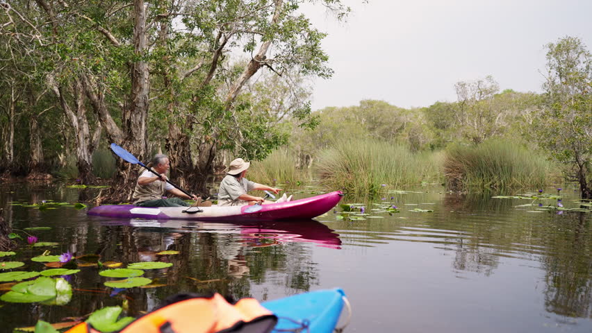 Happy Asian senior couple kayaking in the river on summer holiday vacation. Healthy retired elderly people enjoy and fun outdoor active lifestyle travel nature, sport and rowing a boat in the lake.