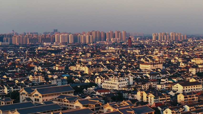 Suzhou. Aerial view of a densely populated urban area during sunset or sunrise, with buildings of varying heights and architectural styles.