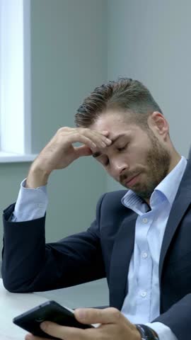 Businessman in formal attire is visibly stressed, with hands covering his face while seated at a desk in a contemporary office, showcasing the challenges of professional life and work pressure