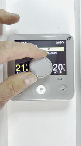 Vertical video - Closeup of a man’s finger and thumb turning the control dial of a modern digital thermostat display, to increase the operating temperature of a heating system in celsius centigrade.