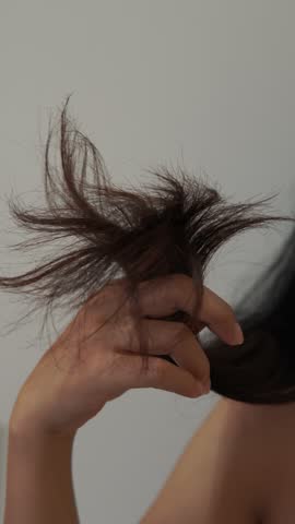 Close up of a young Asian woman showing her dry tangled hair to the camera. Bad hair day concept.
