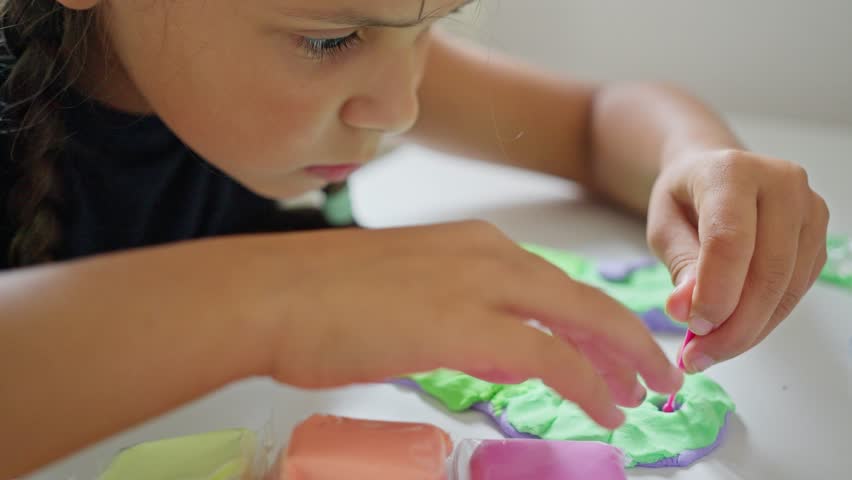 A young child is focused on crafting with vibrant play dough, showcasing their creativity and concentration. Slow motion