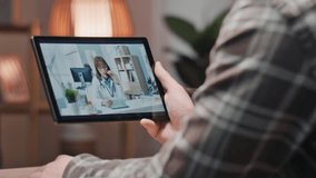 Rear of man holding tablet at home having online consultation with female doctor wearing stethoscope. Male patient receiving remote healthcare advice via telemedicine video call with doc. - Powered by Shutterstock - Get 15% off with code: PIKWIZARD15