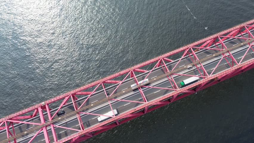 Aerial top-down view of Osaka’s red Minato Bridge on a summer morning, featuring vehicle traffic (trucks, cars) and glistening port water. 4K footage.