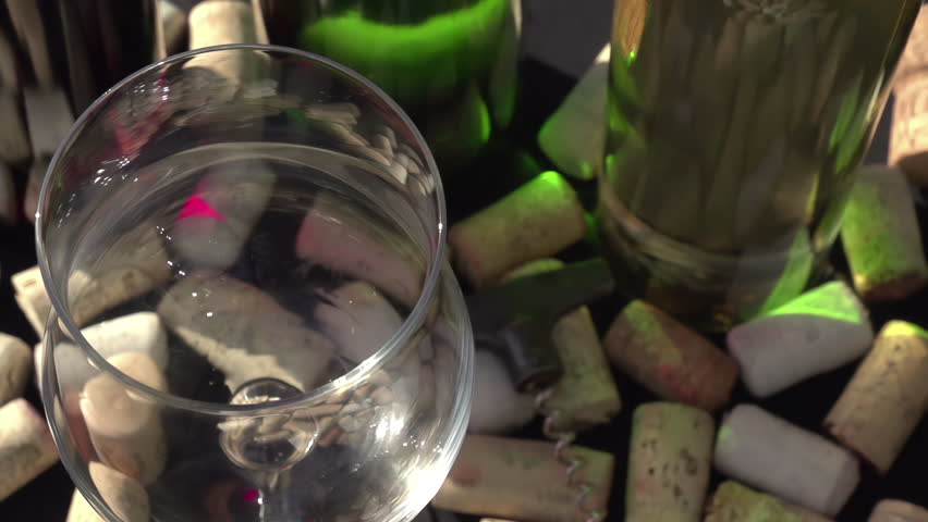 Rose Wine being Poured into a Glass. The camera moves over a glass of rose wine that is poured. Glass on the background of wine bottles and a lot of wine corks. Slow Motion