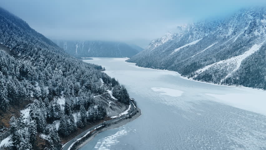 White frozen lake among the spectacular rocks. Snowy pine tree forests cover the mountain slopes. Aerial view.