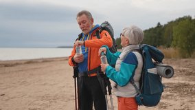 Hiking tourism adventure. Senior couple man woman drinking water enjoying outdoor recreation hiking on beach. Old people backpackers hikers enjoy walking hike trekking active vacation beauty of nature - Powered by Shutterstock - Get 15% off with code: PIKWIZARD15