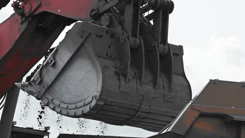Closeup industrial excavator loads coal into back of yellow heavy dump truck in open pit mine, concept mining industry.