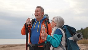 Hiking tourism adventure. Senior couple man woman drinking water enjoying outdoor recreation hiking on beach. Old people backpackers hikers enjoy walking hike trekking active vacation beauty of nature - Powered by Shutterstock - Get 15% off with code: PIKWIZARD15