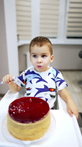 Beautiful baby boy sitting at high chair in front of a bog cake. High angle view at the child enjoying sweet dessert. Vertical video.