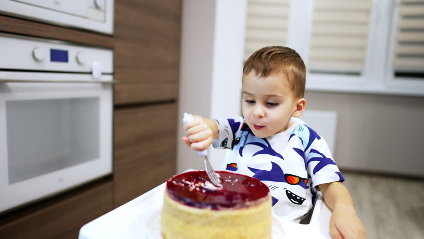 Approaching a baby boy sitting at high chair enjoying a cake. Mom