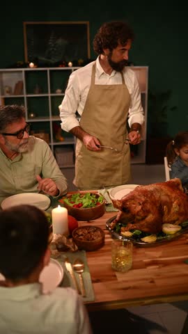 Family gathered around a table, father wearing an apron carving a roasted turkey, enjoying thanksgiving dinner together