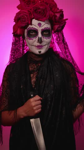 A person in Calavera Catalina makeup, wearing flowers and a veil, presents a knife. Celebrating Day of the Dead, this is perfect for Halloween.