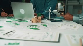 Professionals engage in a collaborative session, analyzing data and discussing sustainable solutions. A wind turbine model adds a creative touch to their innovative workspace. SACTR - Powered by Shutterstock - Get 15% off with code: PIKWIZARD15