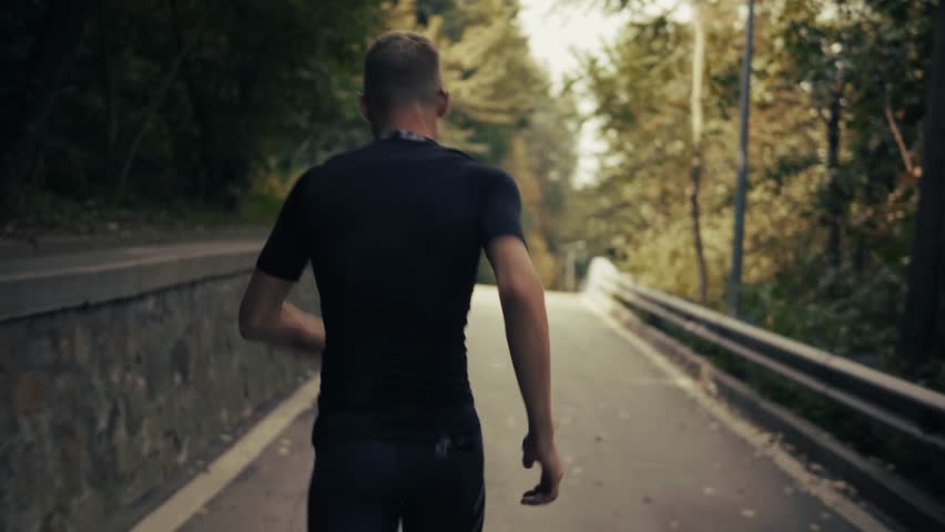 Male Runner Jogging Away On Forest Path Athlete In Motion. Trail Running Adventure, Fitness Training Through Nature. Endurance Sport. Summer Recreation, Active Living, Sportswear Physical Wellness