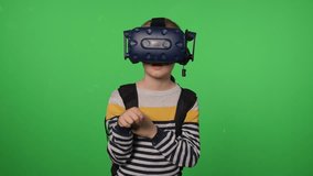 Portrait of a young boy wearing virtual reality glasses, on a green backdrop. He is watching a video, moving his hand through the air, flipping through virtual pages. VR headset. Chroma key. - Powered by Shutterstock - Get 15% off with code: PIKWIZARD15