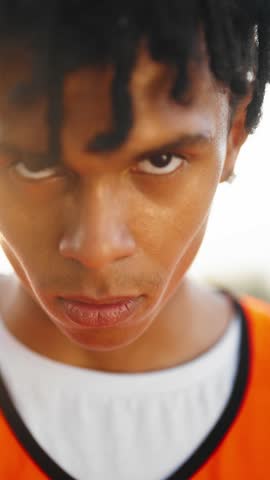 Cinematic portrait of young african american sportsman looking at camera, vertical video. Charismatic and motivated athlete dreaming about win and championship, closeup of face of black teen boy