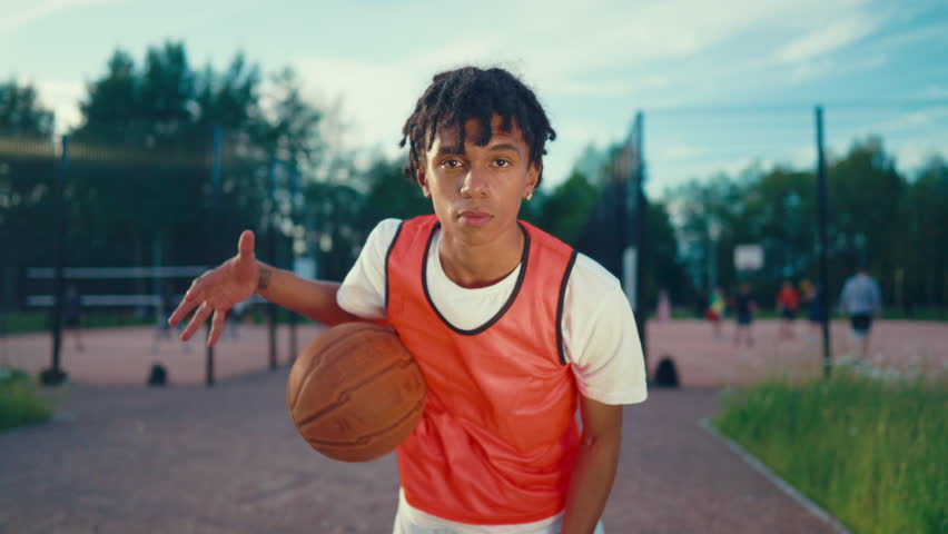 Charismatic african american teen boy playing with ball on streetball court. Portrait of motivated sportive teenager looking at camera when exercising, future champion, sport and hobby for youth