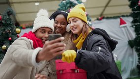 Friends capturing festive moments while taking selfies at bustling christmas market, sharing laughter and joy during holiday season with vibrant urban backdrop - Powered by Shutterstock - Get 15% off with code: PIKWIZARD15