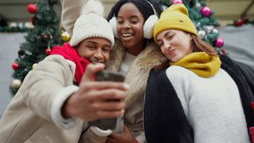 Cheerful multi ethnic friends capturing festive selfies near sparkling christmas market decorations, sharing holiday joy and creating memorable moments - Powered by Shutterstock - Get 15% off with code: PIKWIZARD15