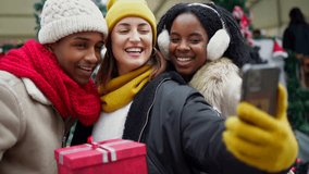 Multicultural friends capturing joyful moment while taking selfie during festive christmas market gathering with holiday spirit and urban winter backdrop - Powered by Shutterstock - Get 15% off with code: PIKWIZARD15