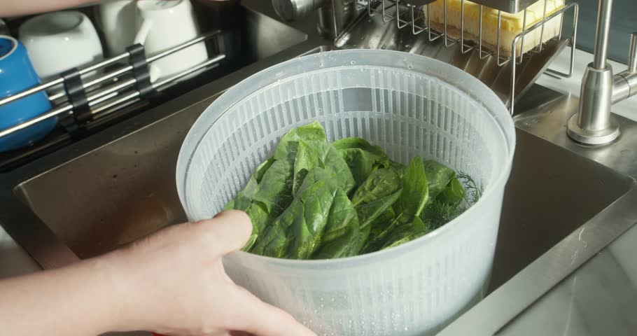 Current of clear tap water falling between green leaves of baby spinach in plastic bowl
