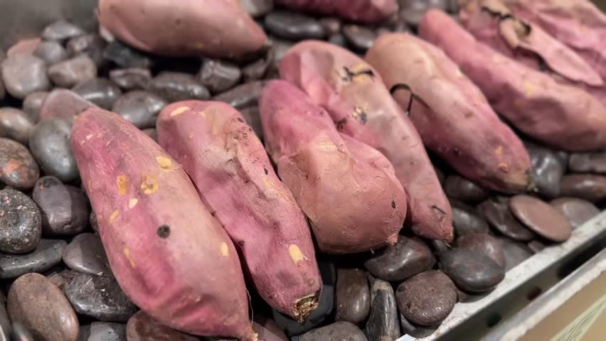 Video of slow-roasted sweet potatoes on hot black stones with textured skin in close-up view